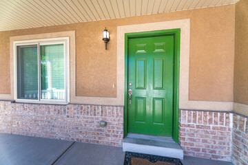 Front porch of a house with green wooden front door and wall lamp