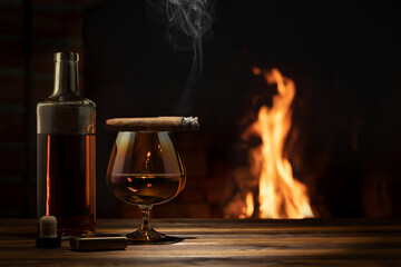 Glass of cognac, a cigar, a bottle on the table near the burning fireplace. Relaxation and enjoyment concept