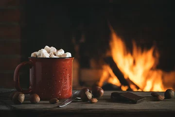 Badkamer foto achterwand Cocoa with marshmallows and chocolate in a red mug on a wooden table near a burning fireplace © Галина Сандалова