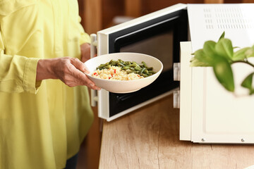 Mature woman heating food in microwave oven - obrazy, fototapety, plakaty
