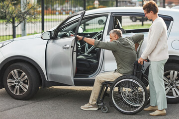 Fototapeta na wymiar Portrait of woman helping man in wheelchair enter car in parking lot outdoors, copy space