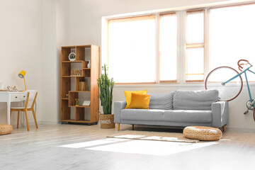 Interior of light living room with grey sofa and modern bicycle