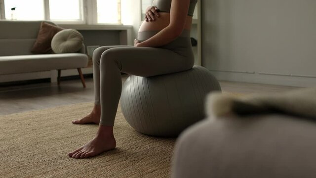 Pregnant woman in sportswear meditates doing exercises on fitball at home. Respiratory gymnastics before childbirth. Large belly with an unborn baby. Healthy image concept. Fitness for pregnant women