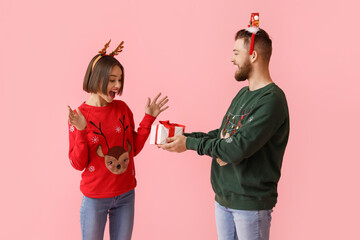 Young woman receiving Christmas gift from her boyfriend on color background
