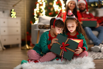 Surprised little brother and sister opening present at home on Christmas eve