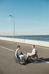 Vertical portrait of adult couple in wheelchairs chatting outdoors and enjoying city life, copy space