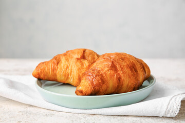 Plate with delicious croissants on light background