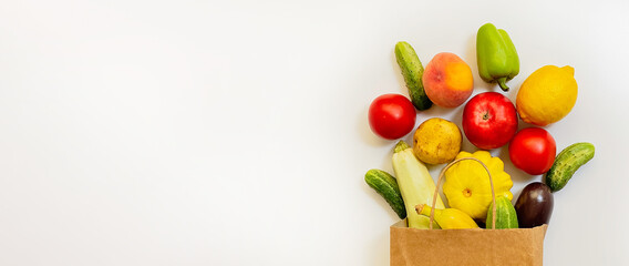 A paper shopping bag with vegetables and fruits, tomato, cucumber, squash, pepper, lemon, eggplant, zucchini, banana, apple, peach on white background