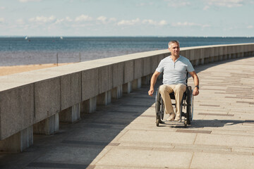 Full length portrait of adult man in wheelchair enjoying outdoors by riverside, copy space