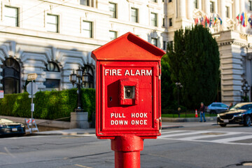 Fototapeta na wymiar Vintage fire alarm red pull box on a city street. Blurred urban background. Close up.