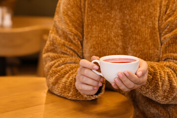 Woman with cup of hot tea at table in cafe, closeup