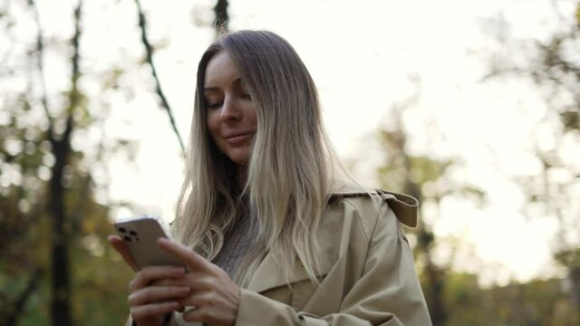 Woman reading messages or surfing internet from phone at autumn park, overview footage