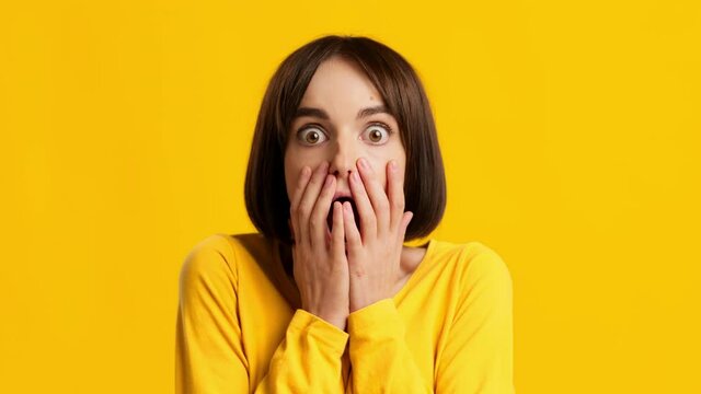 Woman Looking At Camera In Shock Covering Mouth, Yellow Background