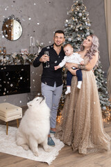 family with little baby boy enjoying their time together with samoyed dog at home near decorated Christmas tree