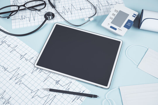 Close up of blue table with blank tablet, stethoscope, cardiogram, pen, other items and mock up place. Doctor's office, workplace and diagnosis concept. 3D Rendering.