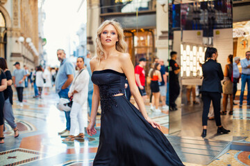 Attractive young blonde girl walking in long black evening dress outdoors