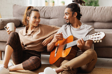 Young smiling african american man musician playing instrumental music on guitar for happy girlfriend