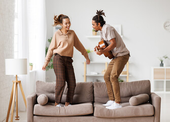 Young funny happy african american couple playing guitar and dancing at home on weekend
