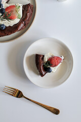 Delicious chocolate flourless cake with strawberry, blueberry and whipping cream on white background. Homemade bakery concept