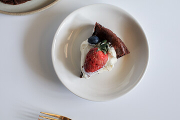 Delicious chocolate flourless cake with strawberry, blueberry and whipping cream on white background. Homemade bakery concept