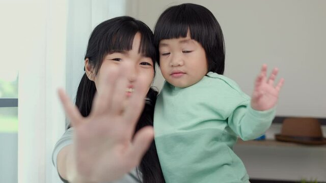 Mom carry son say hi or bye bye to camera feeling happy in the house. Mother holding little boy playing walking around living room at home happy family moment smiling to camera.