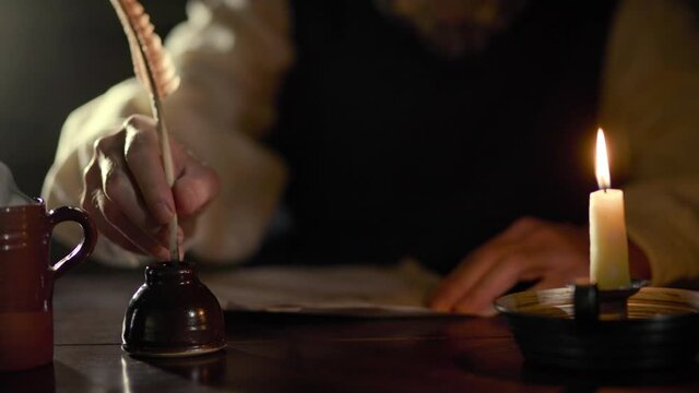 Scene tracks past a man in the 18th century lit by candlelight sitting at a desk with a hot beverage writing with a quill pen.