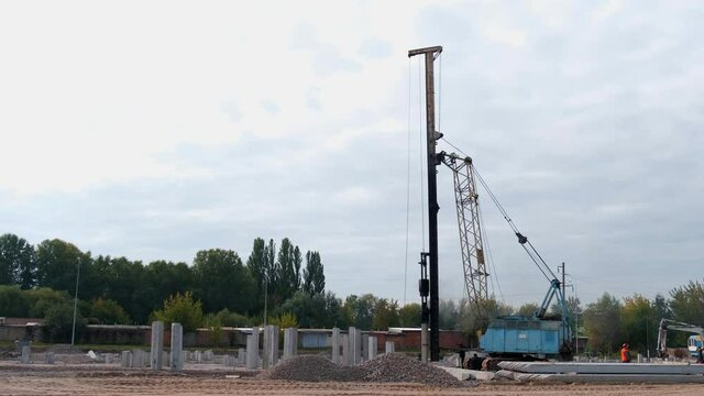 A large vertical pile-driving crane hammers reinforced concrete piles into the ground at a construction site. Time lapse.