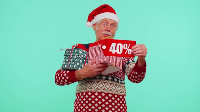 Mature grandfather in Christmas sweater showing gift box, 40 Percent discount inscriptions banner text. Black Friday. Good holiday low prices for shopping. Blue studio wall background. Happy New Year
