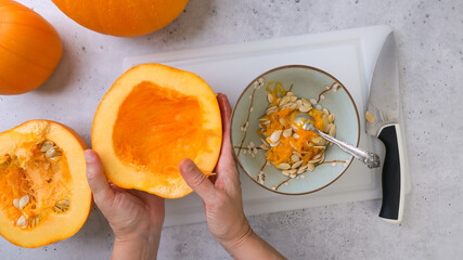 Woman scoops soft flesh and seeds out of the middle of pumpkin, flat lay