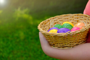 Fototapeta na wymiar Easter Egg Hunt. Easter eggs in a basket in children's hands on green grass background. Collecting eggs. Religious holiday tradition. Colorful easter eggs.Easter holiday symbol