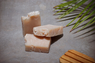 Handmade coconut and vanilla soap bars on grey concrete background. Featured by a palm leaf and natural light.