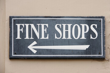 Signage on a building wall with an arrow pointing the direction to FINE SHOPS
