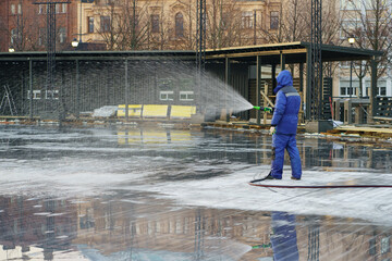 City preparing for winter: worker in uniform hold water hose filling area for ice rink, outdoor activities in urban, winter sport games and hockey competition. Wintertime season preparation concept