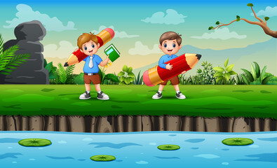 Obraz na płótnie Canvas Happy school boys holding big pencil by the lake