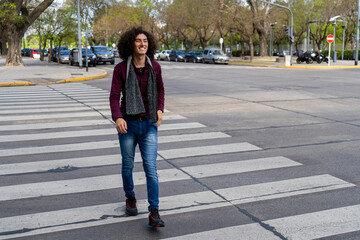 portrait of a young Latin man with curly hair crossing the street on the pedestrian path.