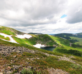 A look at the alpine lake with snow on the shores and slopes of high hills under a dark cloudy sky.