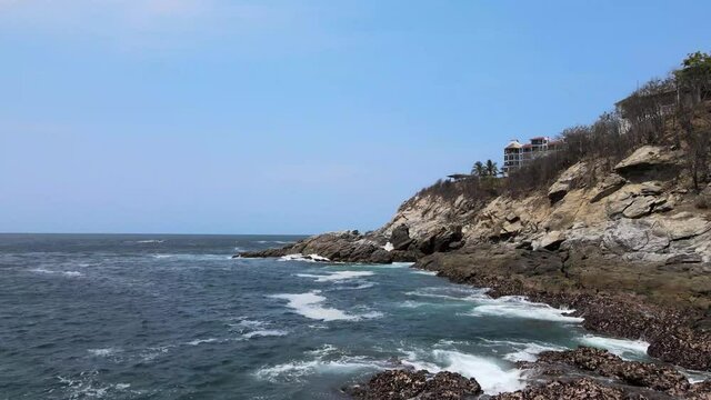 Pull front above rocks and waves with view of cliff and small hotel in Oaxaca, Mexico