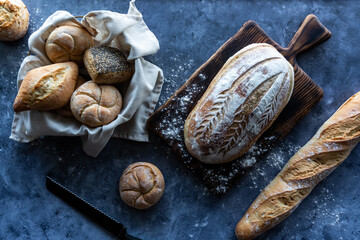 Top down view of various sourdough bread and buns, against a dark background.