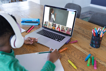 African american boy using laptop for video call, with diverse elementary school pupils on screen