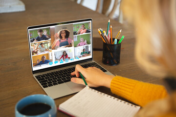 Fototapeta na wymiar Caucasian woman using laptop for video call, with smiling diverse elementary school pupils on screen