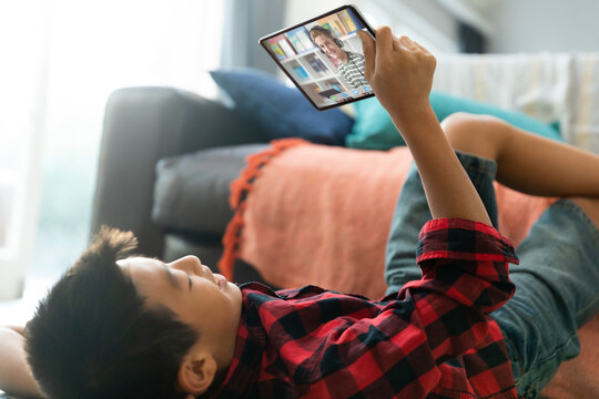 Smiling asian boy using tablet for video call, with smiling elementary school pupil on screen