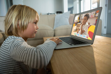 Caucasian boy using laptop for video call, with bored elementary school pupil on screen