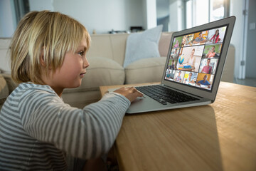 Caucasian boy using laptop for video call, with smiling diverse elementary school pupils on screen