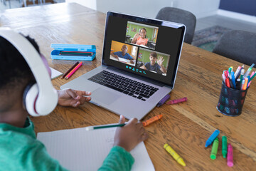 African american boy using laptop for video call, with diverse elementary school pupils on screen
