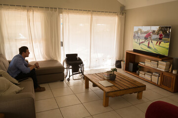 Caucasian disabled man sitting at home watching cricket match on tv