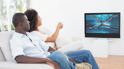 Rear view of african american couple sitting at home together watching swimming competition on tv