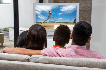 Rear view of family sitting at home together watching athletics event on tv