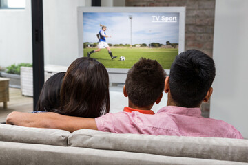 Rear view of family sitting at home together watching football match on tv