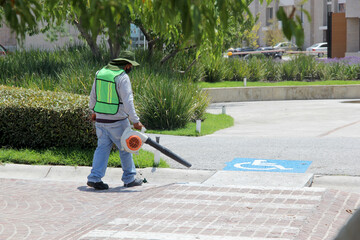 Man wearing a mask, high visibility safety vest and hat works cleaning the streets with a leaf...