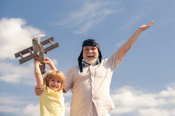 Young grandson and old grandfather with toy jetpack plane against sky. Child pilot aviator with plane dreams of traveling.